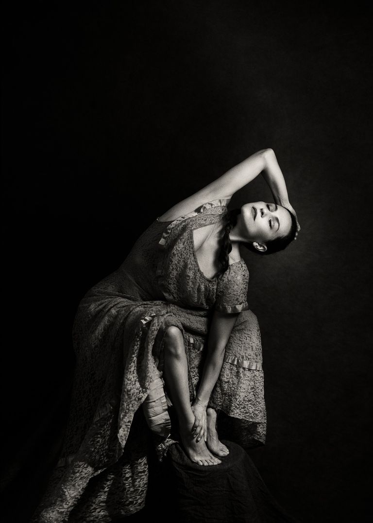 Bailarina posando de lado con un vestido largo y una trenza con un codo doblado hacia arriba y una mano tocándose el tobillo